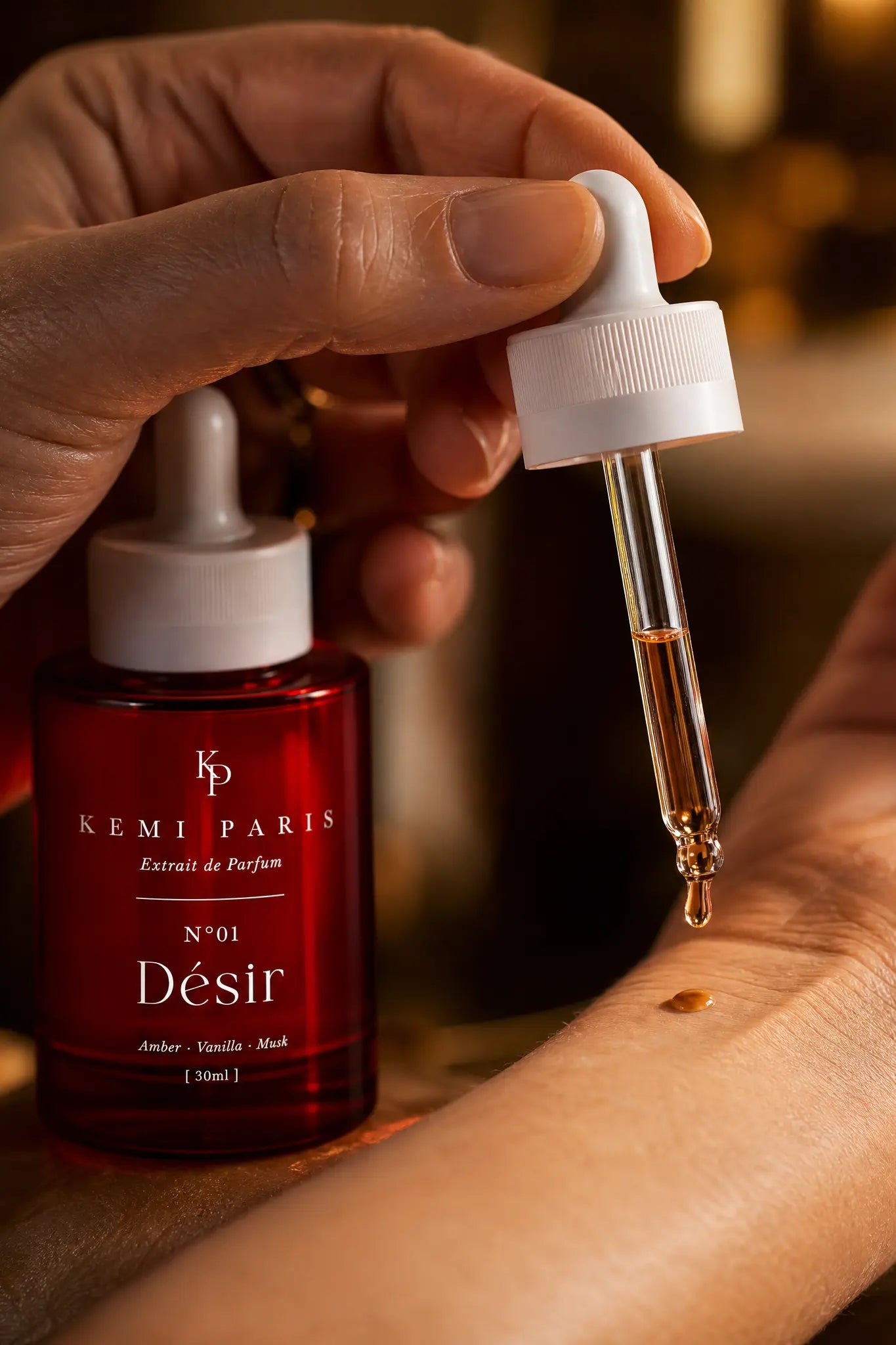 A hand holding the glass dropper, one amber drop falling to the wrist